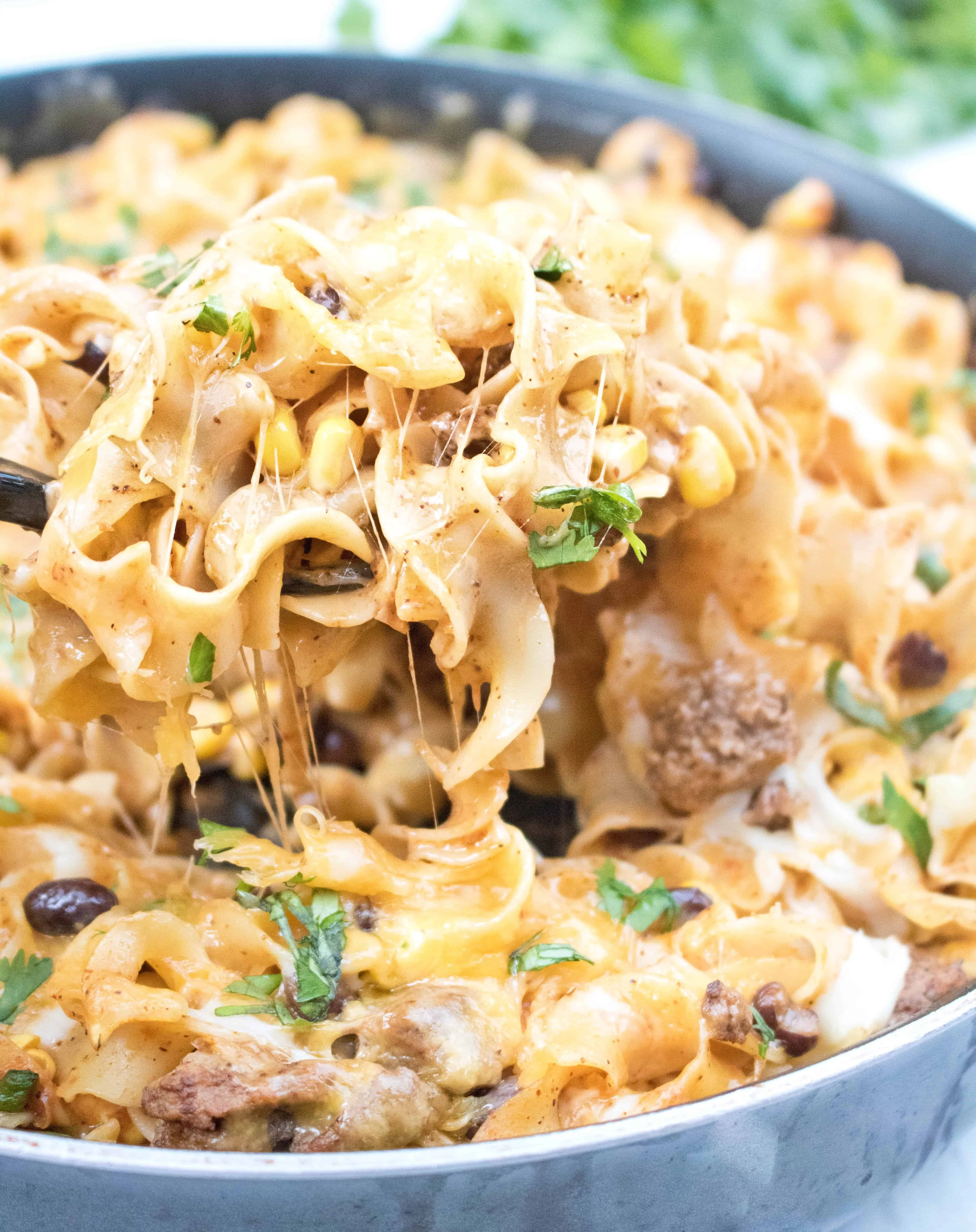 a spoon scooping out cheesy pasta from a pan.