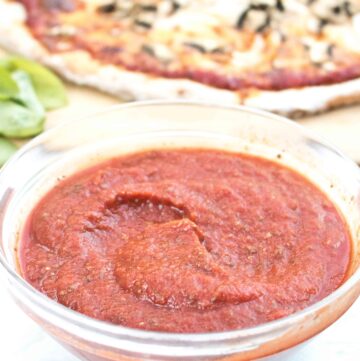 bowl of pizza sauce in front of a pizza