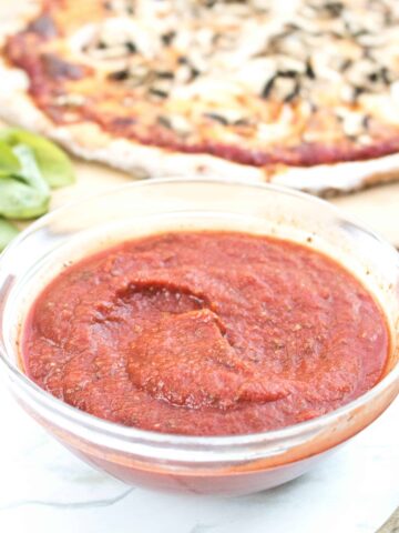 bowl of pizza sauce in front of a pizza