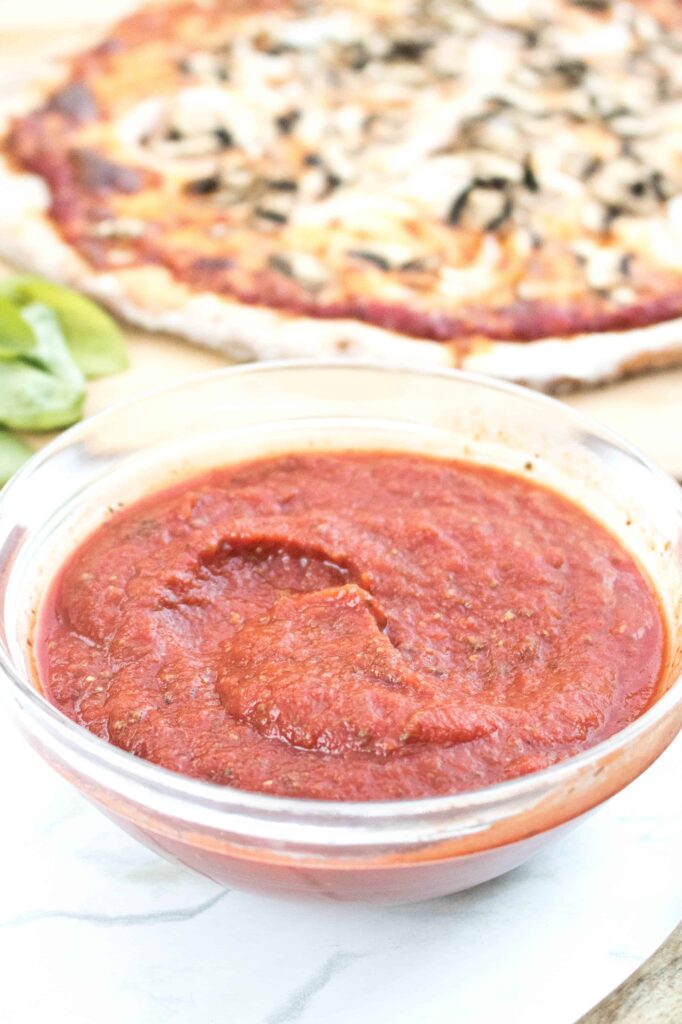 bowl of pizza sauce in front of a pizza