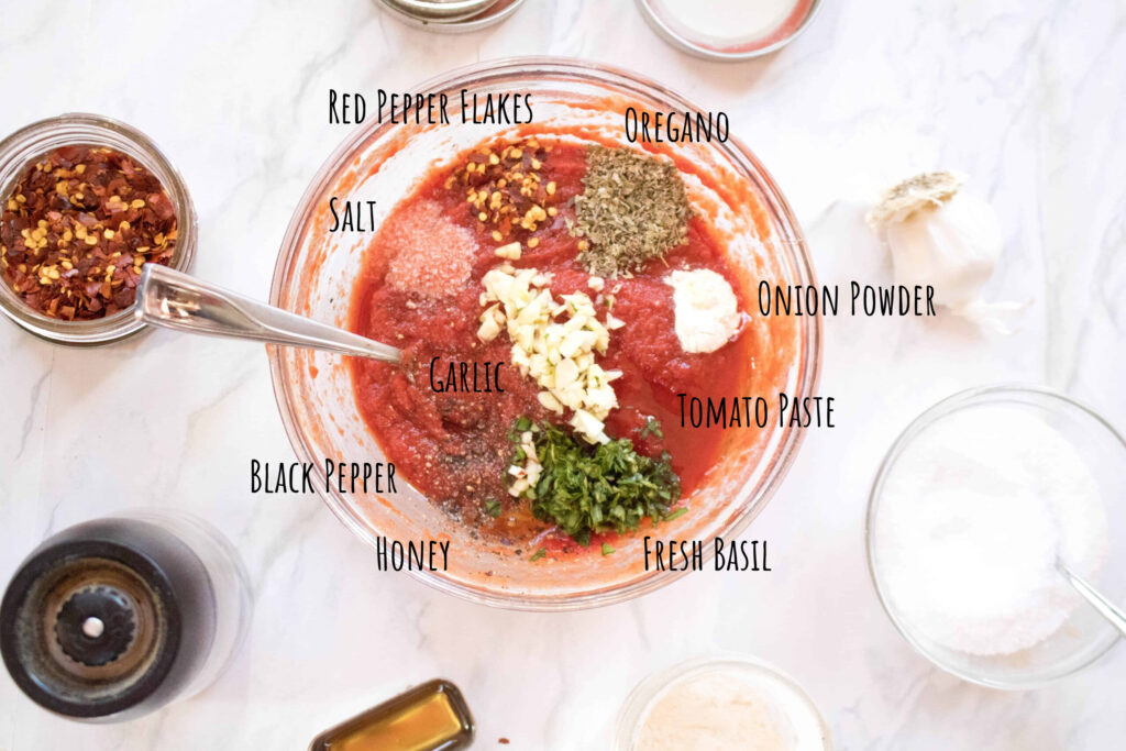 bowl with tomato paste, oregano, garlic, salt, onion powder, red pepper flakes, fresh basil, garlic, honey, black pepper