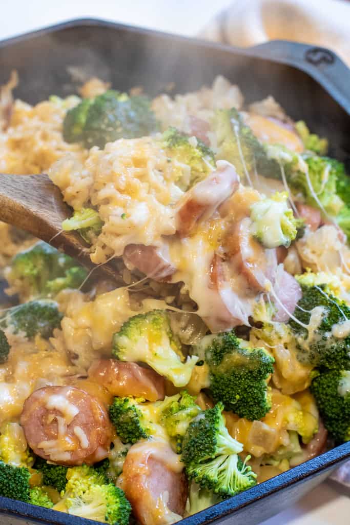 a spoon scooping out some rice with kielbasa and broccoli and cheese.