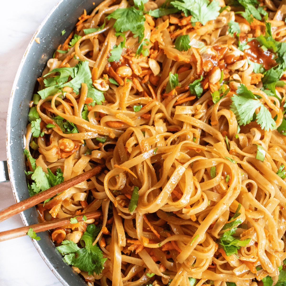 a pan with cooked noodles and cilantro, carrots, peanuts