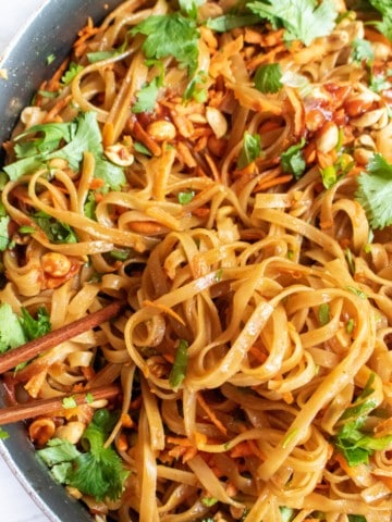 a pan with cooked noodles and cilantro, carrots, peanuts