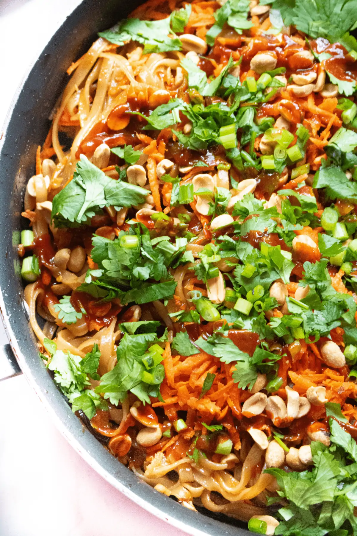 a pan with noodles, carrots, cilantro, and peanuts.