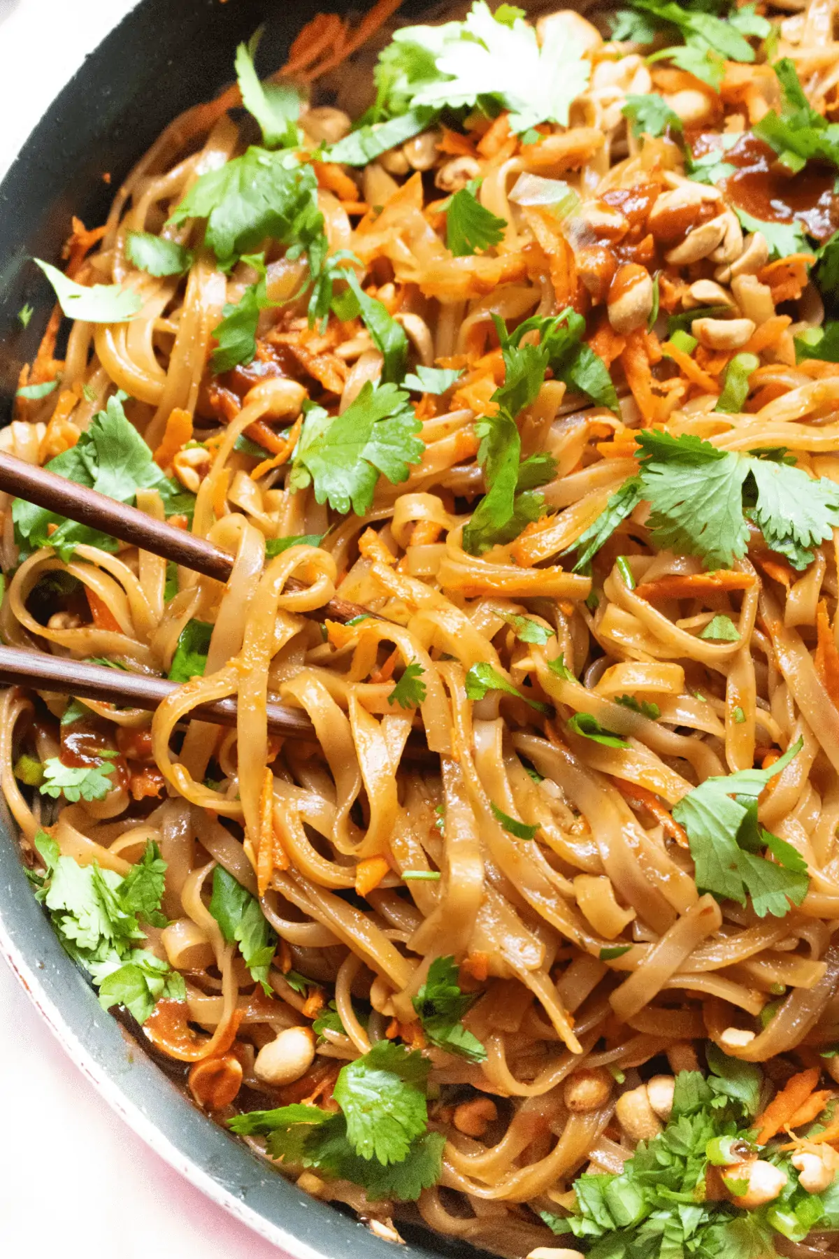 a pan with cooked noodles and cilantro, carrots, peanuts.