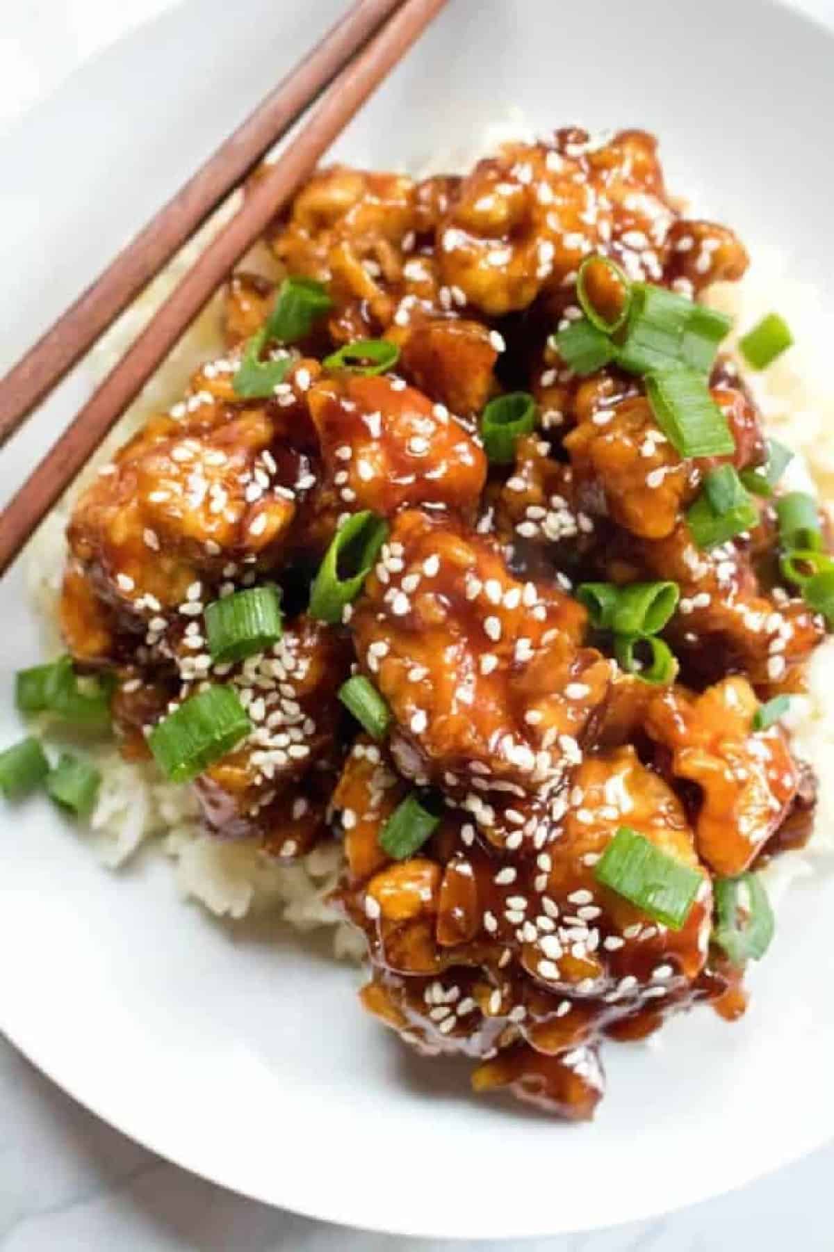 a plate of sesame chicken with chopsticks with Pinterest pin text.