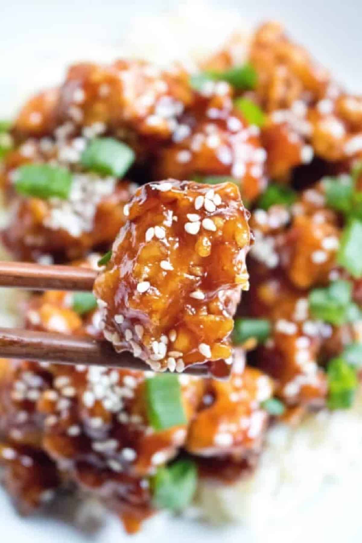 cooked crispy sesame chicken held up by chopsticks.