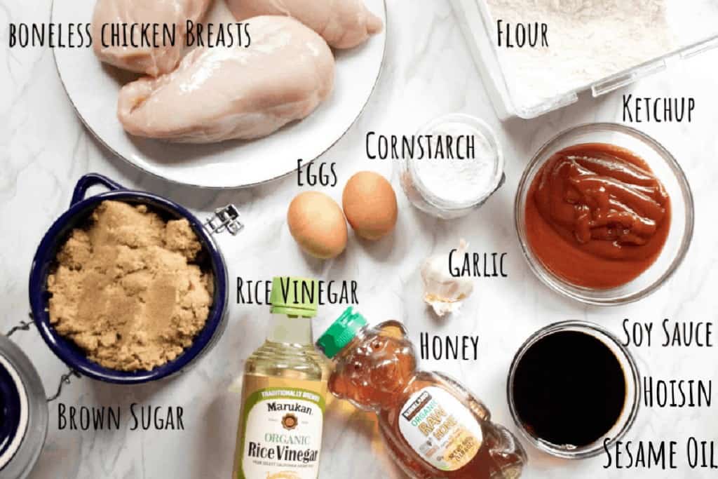 raw chicken breasts, flour, ketchup, cornstarch, eggs, garlic, soy sauce, honey, rice vinegar, brown sugar on a counter.