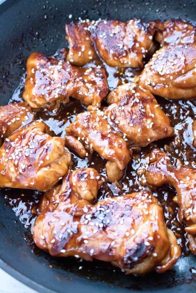 A pan with cooked chicken thighs in a sauce and sesame seeds