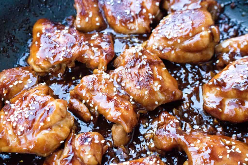 A pan of cooked chicken thighs in a thick sauce with sesame seeds 