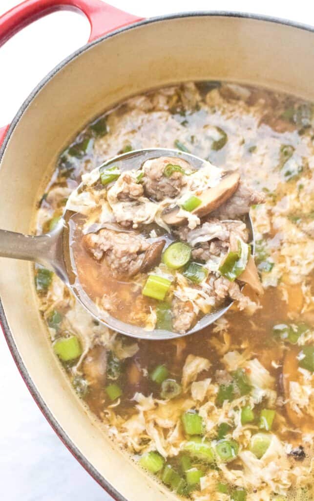 a soup ladle scooping our mushroom pork soup from a dutch oven.