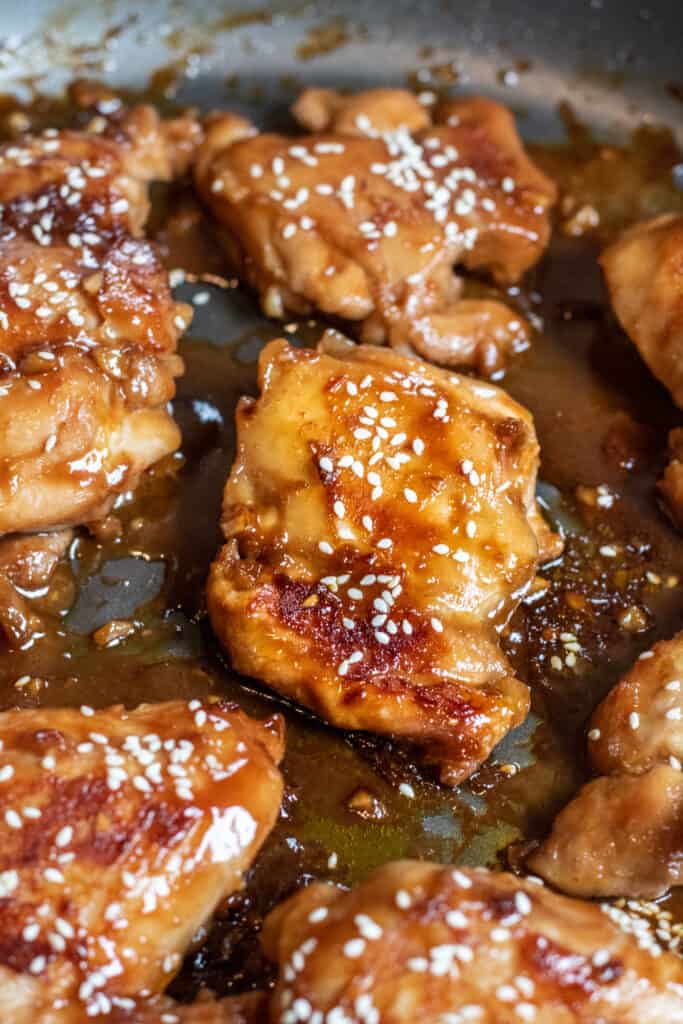 a pan of cooked glazed chicken thighs topped with sesame seeds.