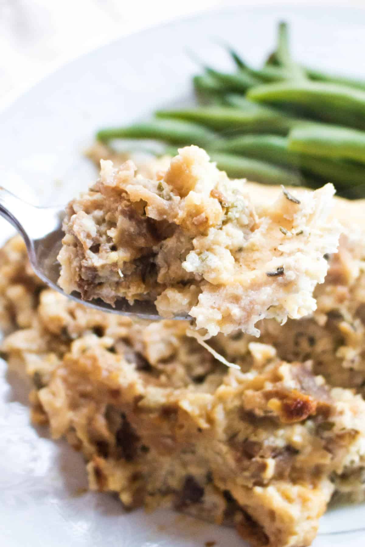 a fork holding up a bite of chicken and stuffing in front of a plate.