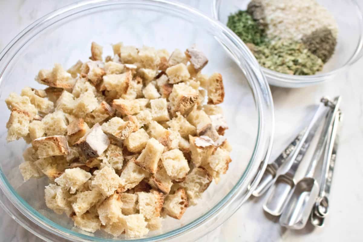 a bowl of cubed stale bread next to a bowl of spices and measuring spoons.