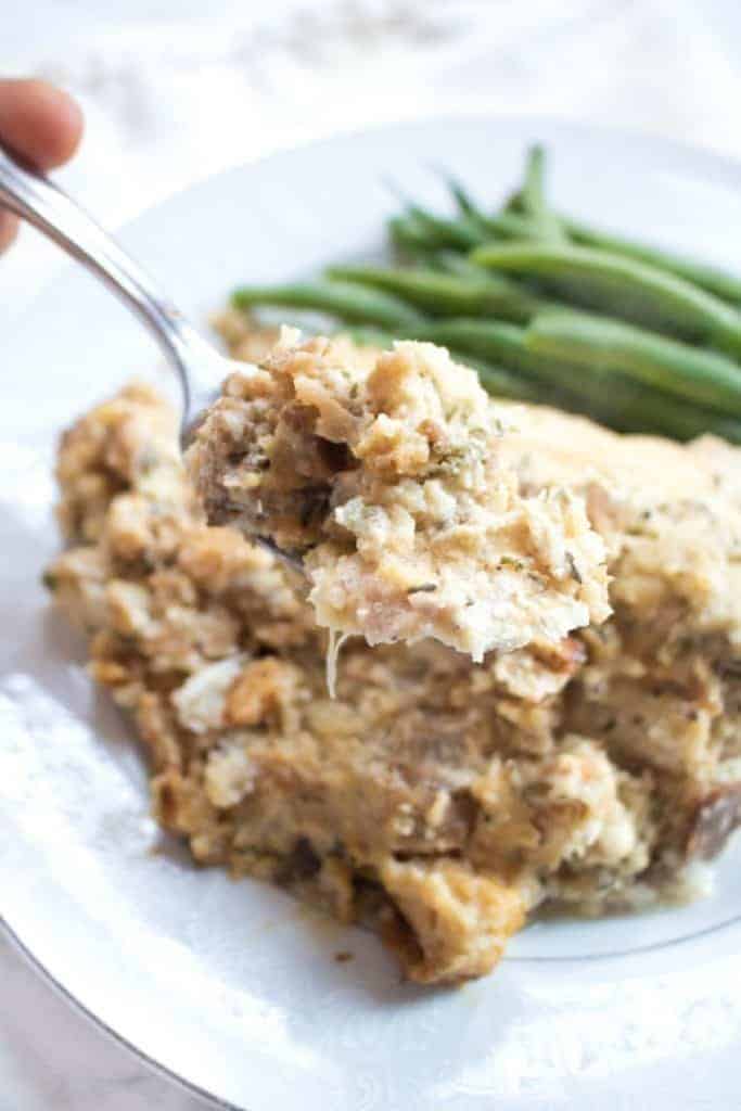 a fork holding up a bite of chicken and stuffing in front of a plate.