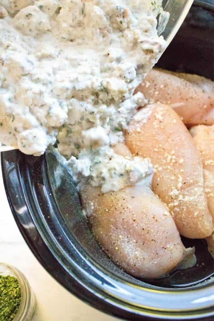 raw chicken in a crock and cream of chicken soup being poured in.