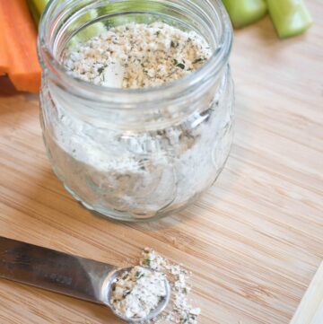 a small jar with dry ranch mix and a measuring spoon on a cutting board with carrots and celery