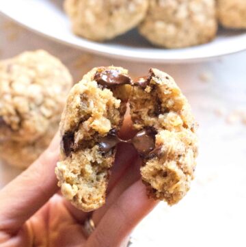 a hand holding a cookie with melted chocolate chips in half