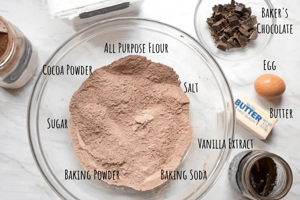 a bowl with mixed dry ingredients and butter, egg, baker's chocolate, and vanilla extract on counter.