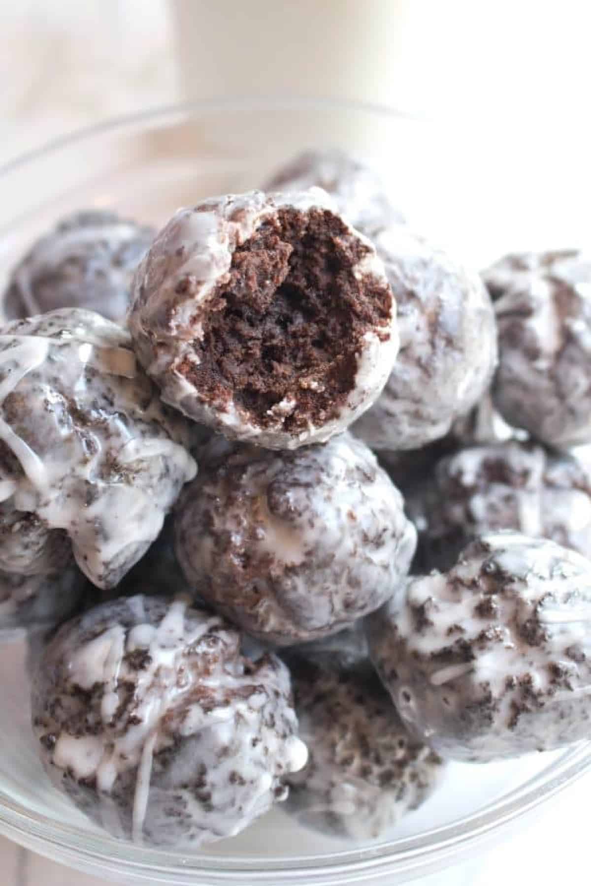 a bowl of chocolate munchkins with one with a bite taken out.