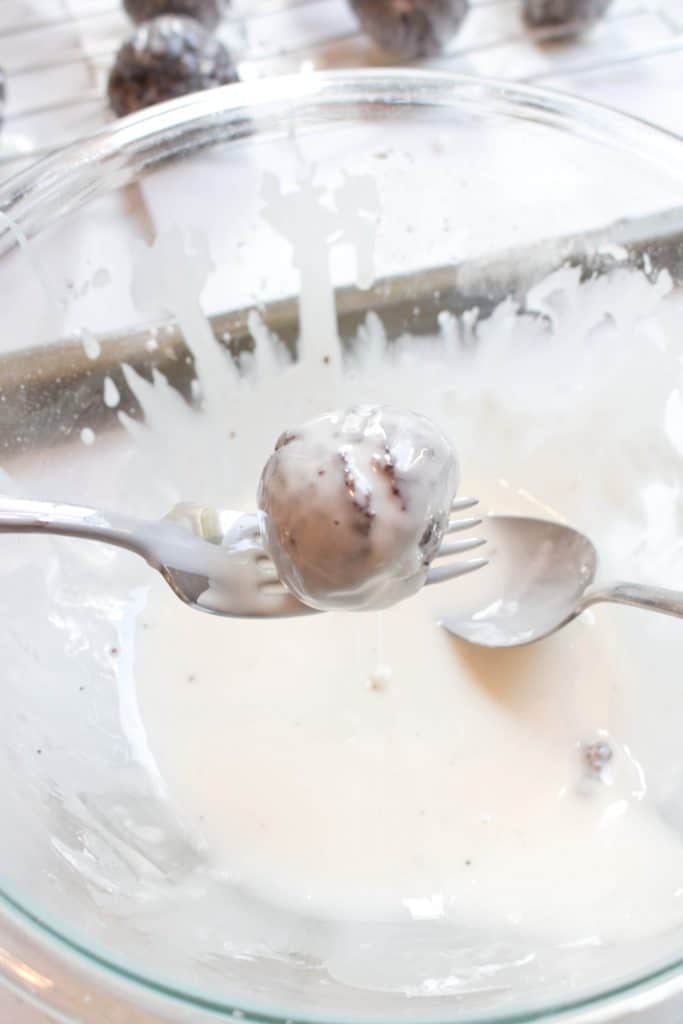 dipping baked chocolate donut holes in glaze with a fork.
