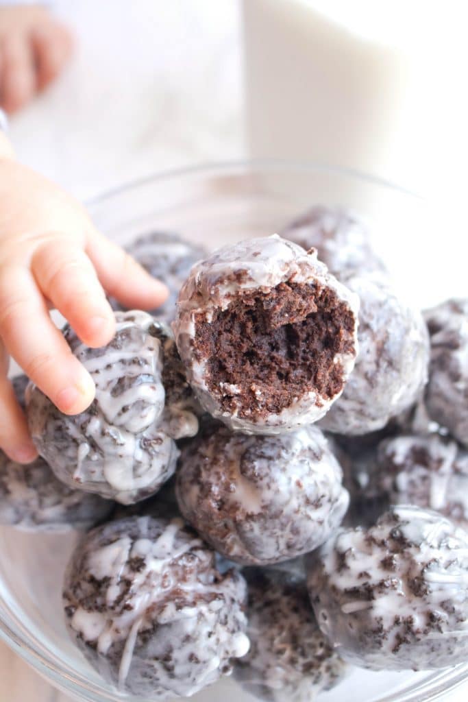 glazed chocolate donut holes in a bowl one with a bite taken out.
