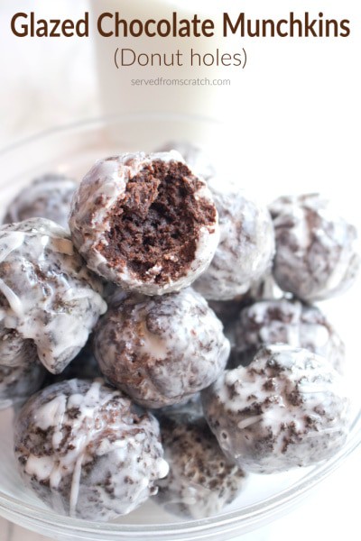 a bowl of glazed chocolate donuts one with a bite taken out