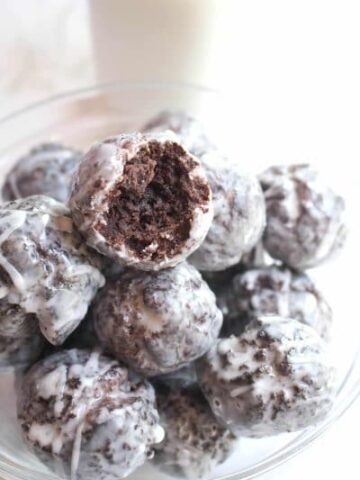 a bowl of glazed chocolate donuts one with a bite taken out