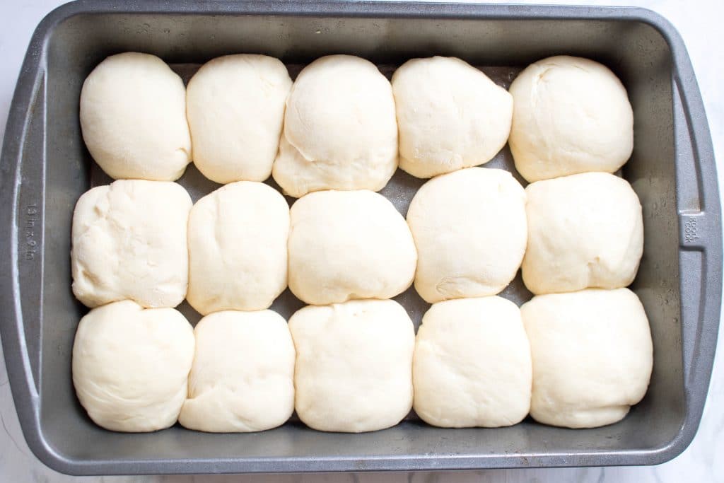 15 risen balls of dough in a pan.