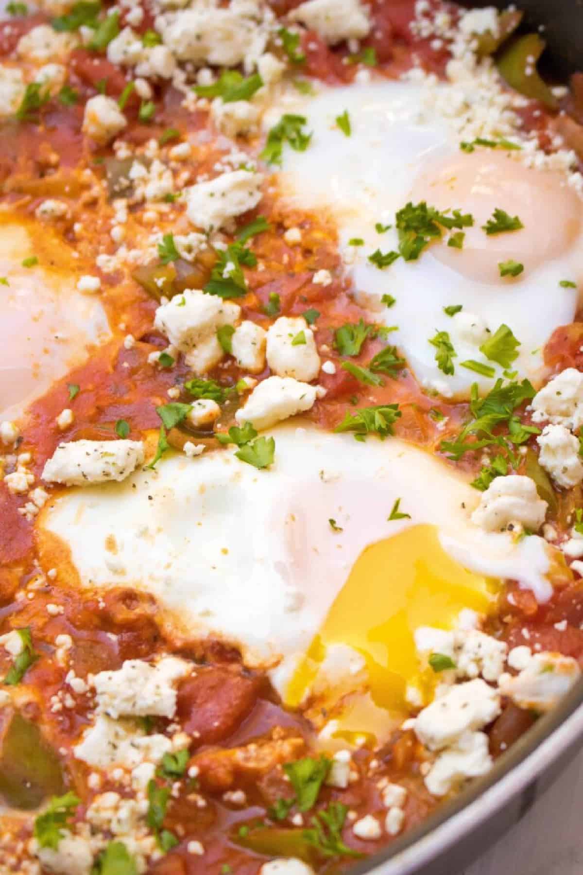 a pan with baked eggs and tomatoes and feta with a runny yolk.