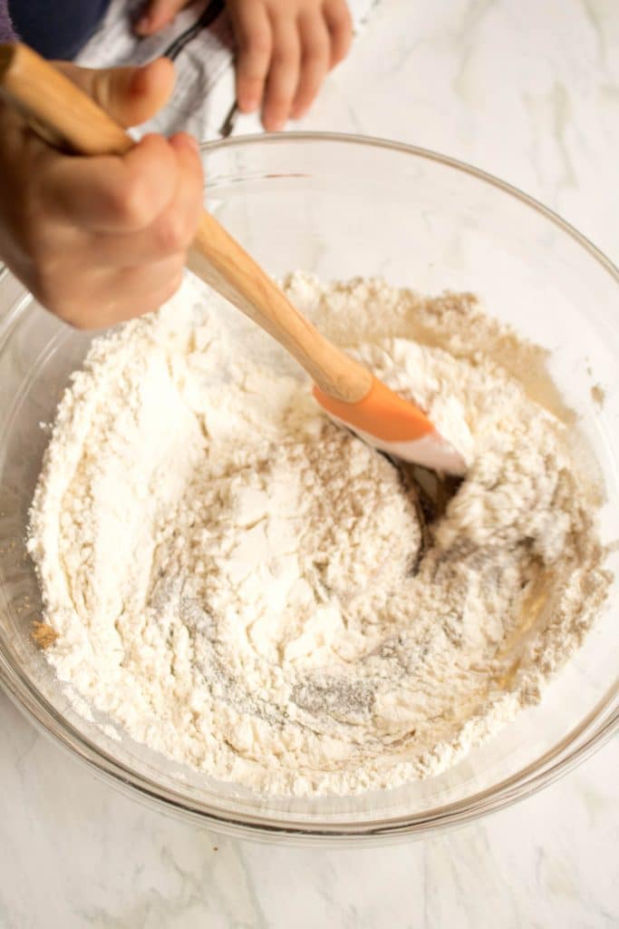 an overhead of a hand mixing a bowl of flours
