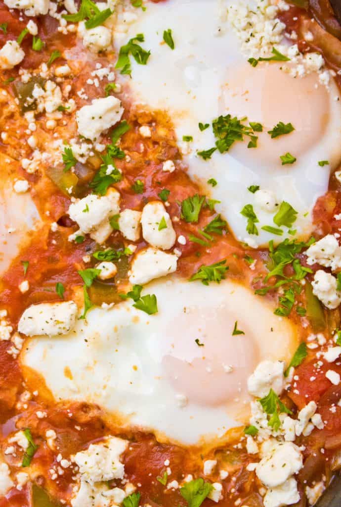 a close up of poached eggs in a tomato sauce with feta cheese