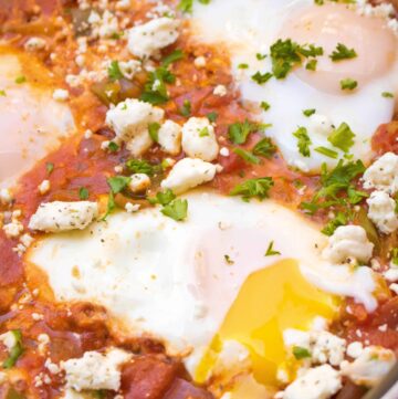 a pan with baked eggs and tomatoes and feta with a runny yolk.