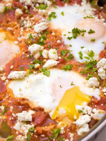 a pan with baked eggs and tomatoes and feta with a runny yolk.
