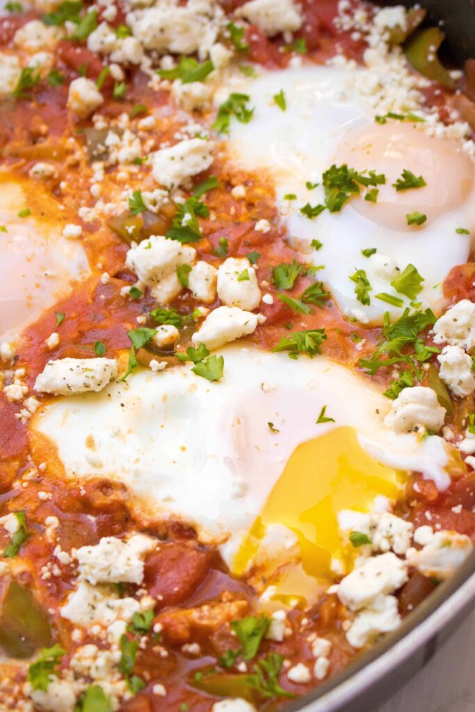 a close up of poached eggs in a tomato sauce with feta cheese