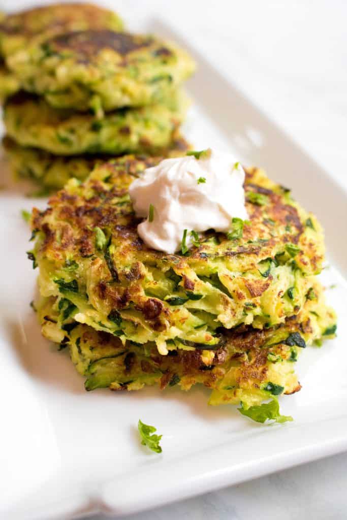 stacked zucchini fritters topped with sour cream on a plate.