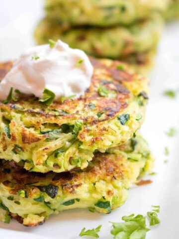 a close of up of stacked zucchini fritters topped with sour cream