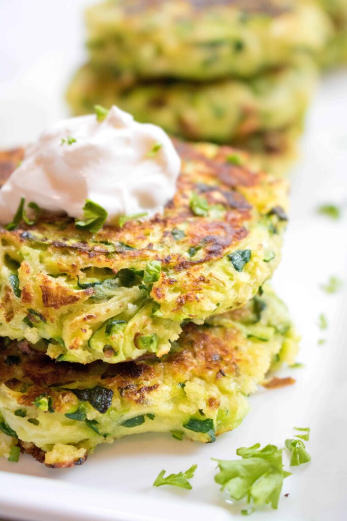 stacked zucchini fritters topped with sour cream on a plate.