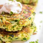a stack of cooked zucchini fritters with a dollop of sour cream on top.