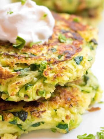 a stack of cooked zucchini fritters with a dollop of sour cream on top.