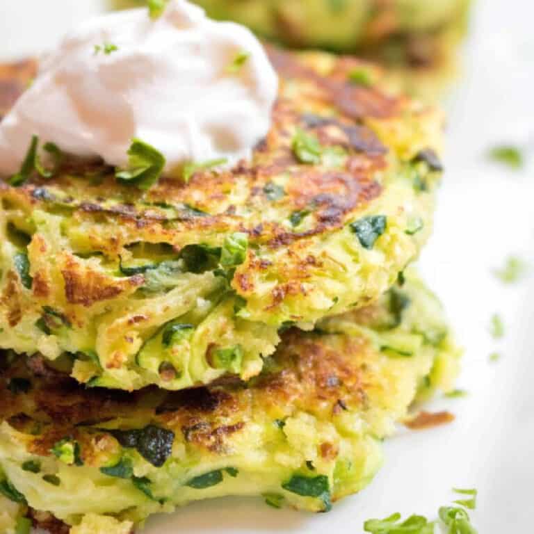 a stack of cooked zucchini fritters with a dollop of sour cream on top.