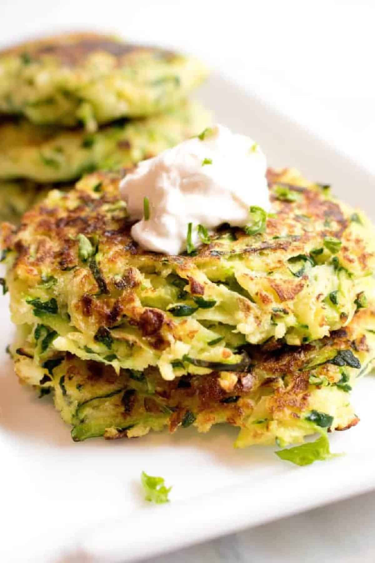 a stack of cooked zucchini fritters with a dollop of sour cream on top.