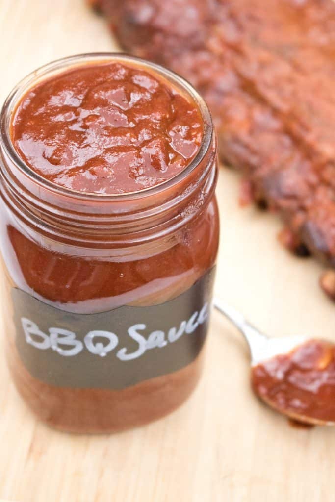 an open mason jar of bbq sauce in front of ribs.