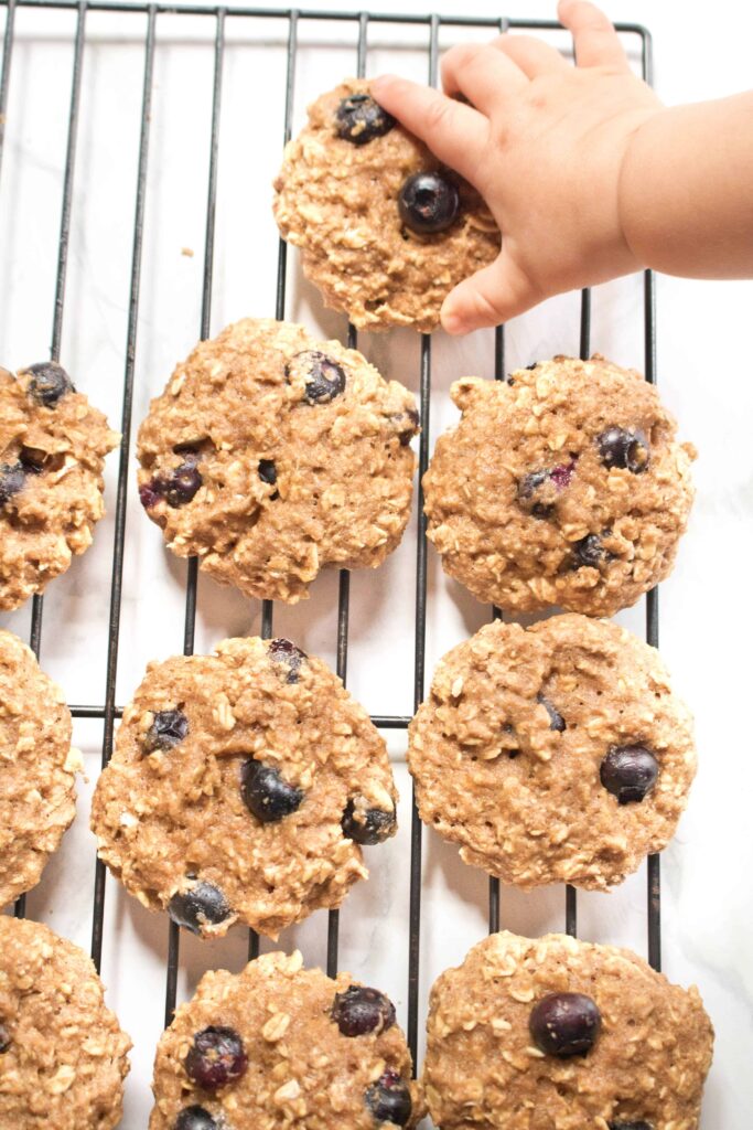 baked blueberry oatmeal cookies on a cooling rack with baby hand grabbing one