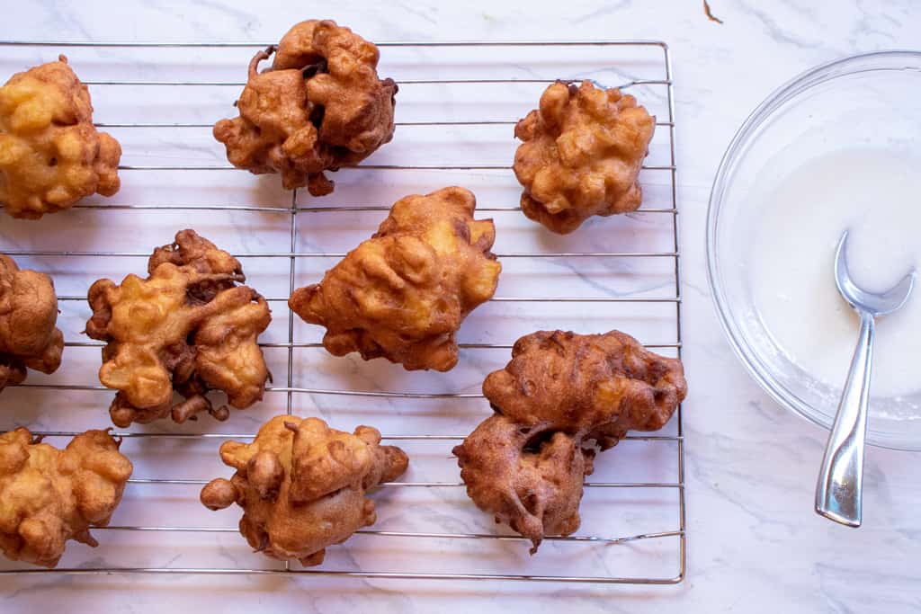 apple fritters cooling on a rack next to a bowl of glaze