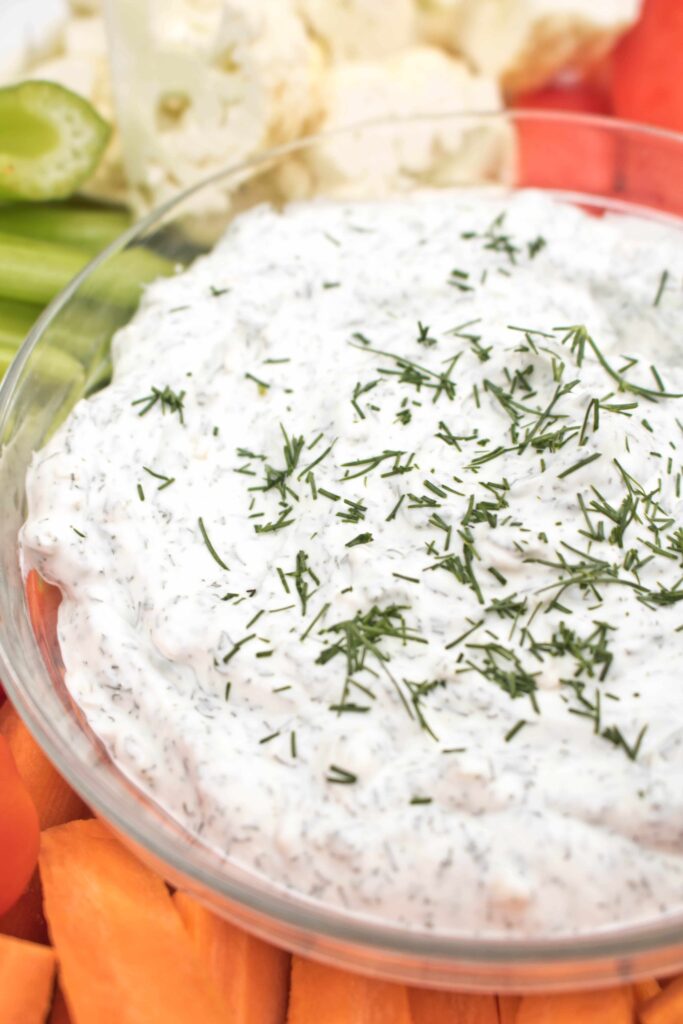 a bowl of dill onion dip surrounded by veggies.