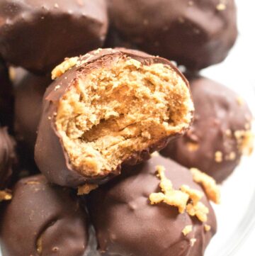 a hand holding a chocolate covered butterfinger ball with a bite taken out