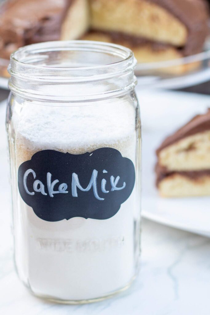 A mason jar of cake mix in front of a cake