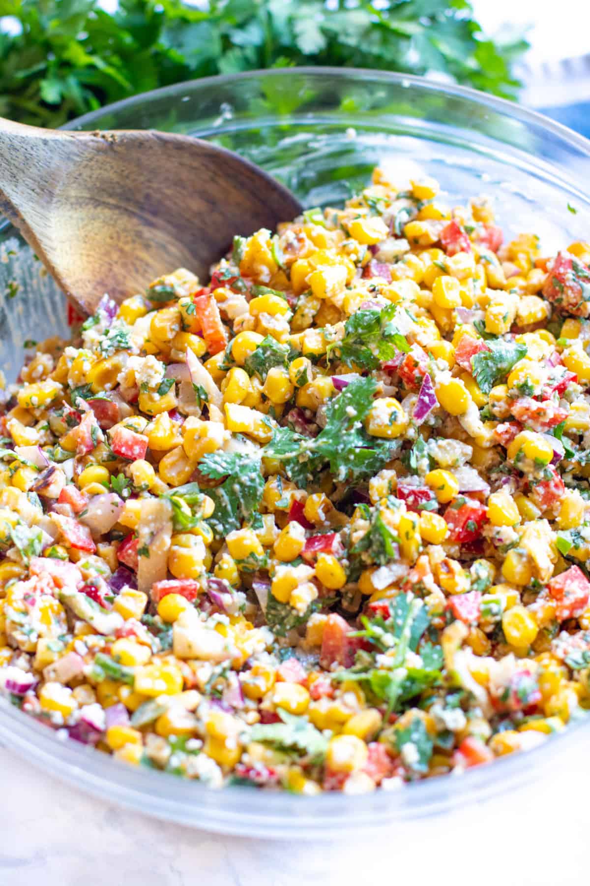a big bowl of Mexican Street Corn Salad with a wooden spoon in it.